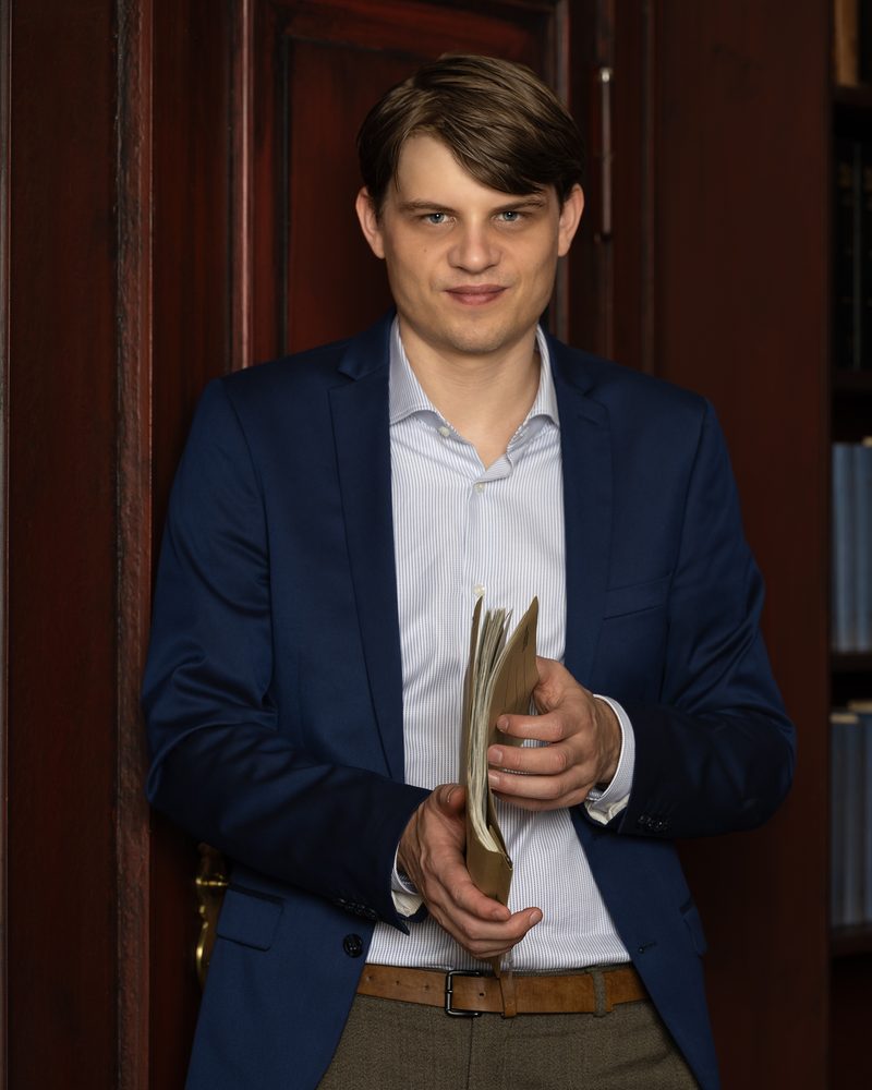 Rechtsanwalt Richard Mertens mit einer Akte in der Hand vor Bücherregalen