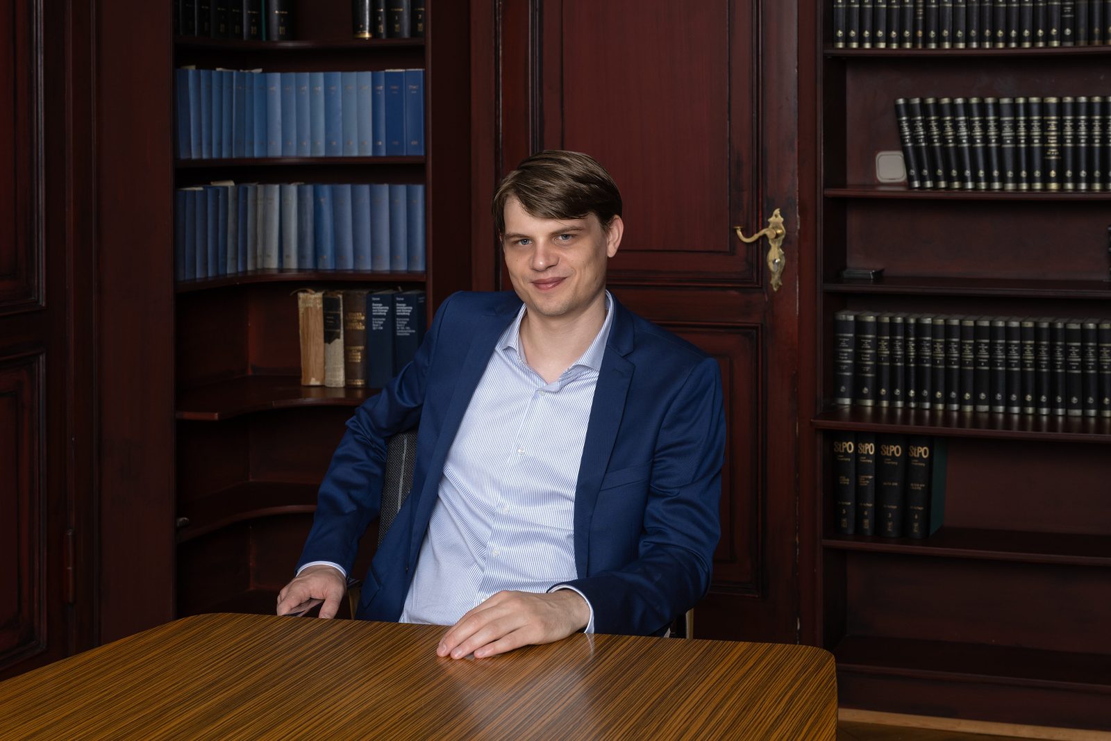 Rechtsanwalt Richard Mertens am Besprechungstisch vor Bücherregalen mit juristischer Fachliteratur